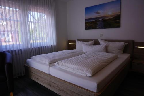 uma cama com lençóis brancos e almofadas num quarto em Pension Julia 2 em Norden