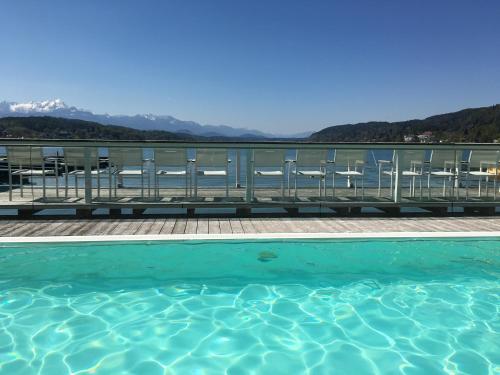 a swimming pool with chairs and mountains in the background at See & You Familienwohnung mit Hotelanbindung in Pörtschach am Wörthersee