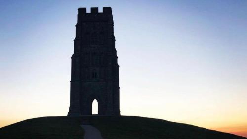 a clock tower on a hill with the sunset in the background at Inn Glastonbury - Self Catering in Glastonbury