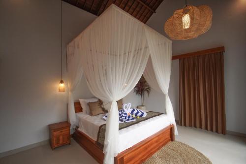a bedroom with a canopy bed with white curtains at Nick Villa in Ubud