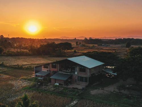 a house in a field with the sunset in the background at SuanGlangNa in Phrae
