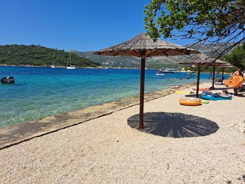 ein Strand mit zwei Sonnenschirmen und dem Wasser in der Unterkunft Enjoy Vrbovica in Korčula