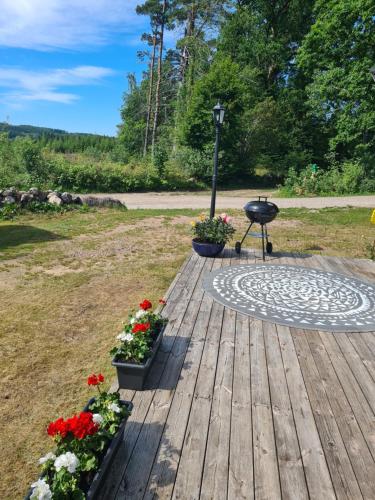 um deque de madeira com flores em vasos e um grelhador em Stuga i naturen em Simlångsdalen