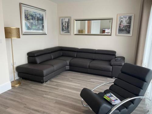 uma sala de estar com um sofá preto e uma cadeira em MODERN 4 BEDROOM HOUSE WITH GARDEN & PARKING em Swanscombe
