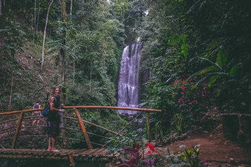 Eine Frau, die auf einer Brücke vor einem Wasserfall steht. in der Unterkunft Desa Eko in Munduk