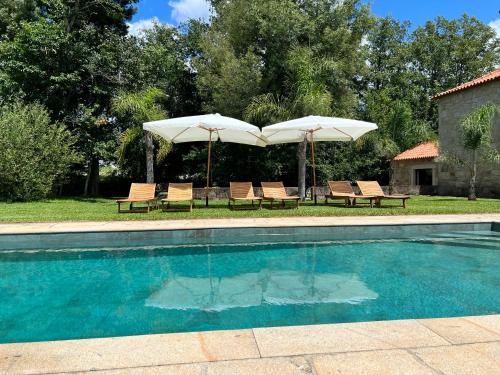 a swimming pool with two umbrellas and two chairs at Quinta do Moinho da Ínsua in Ponte de Lima
