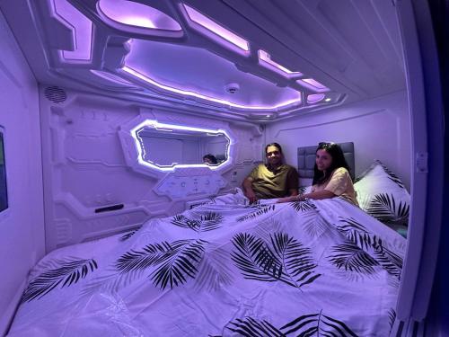 mężczyzna i kobieta siedzący na łóżku w fioletowym pokoju w obiekcie GOOD VIBES ONLY Capsule Hostel Malaga w Maladze