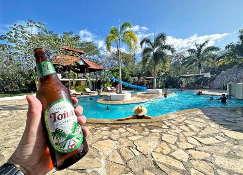 a person holding a bottle of beer in front of a swimming pool at Surf Ranch Hotel & Resort in San Juan del Sur