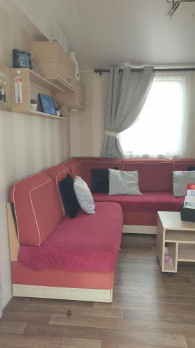 un divano rosso in un soggiorno con finestra di Sylvie propriétaire du mobil-home " Camping de la Chanterie" a Saint-Pair-sur-Mer