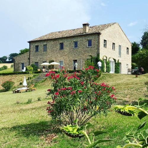 a large stone house with red flowers in front of it at Il Giardino nella Valle in Belvedere Ostrense
