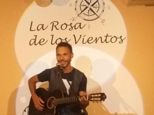 Un uomo che suona la chitarra davanti a un cartello di Rosa de los Vientos a Cadice
