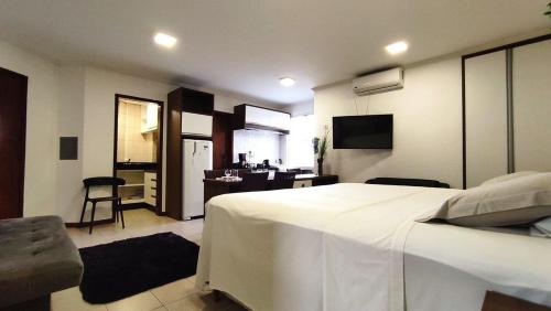 a bedroom with a large white bed and a kitchen at Lindos Studios Centro/Wifi/Garagem in Foz do Iguaçu
