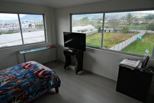 a room with a bed and a tv and two windows at Paraíso San Marcos in San Miguel de Salcedo