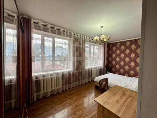 a bedroom with a bed and a table and windows at Hostel 4U in Bishkek