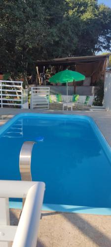 een blauw zwembad met een groene parasol en stoelen bij Casa Di Gaya in Cabo Frio