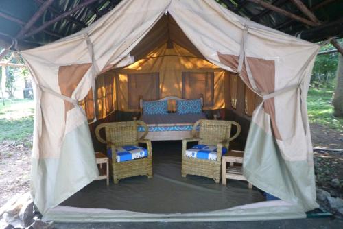 a tent with a bed and wicker chairs in it at Banda Island Resort and Campsite in Kalangala