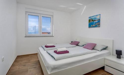 biała sypialnia z dużym łóżkiem z fioletowymi poduszkami w obiekcie Apartmani Grgić on the adress Branka Fučića 96 w mieście Malinska