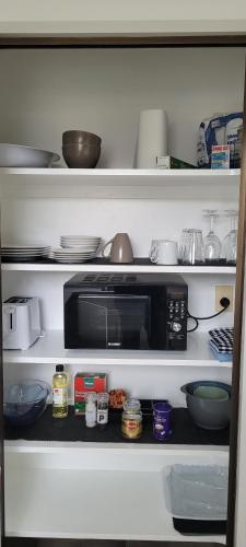 a kitchen shelf with a microwave and bowls and dishes at Couples Retreat in Reefton