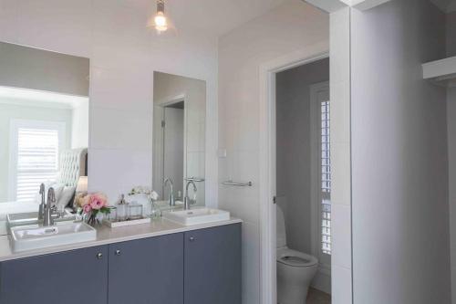 a white bathroom with two sinks and a toilet at WineCountry Holiday House in Branxton
