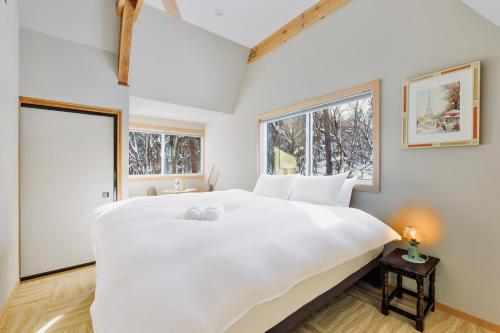 ein großes weißes Bett in einem Zimmer mit zwei Fenstern in der Unterkunft Piccolo House in Hakuba