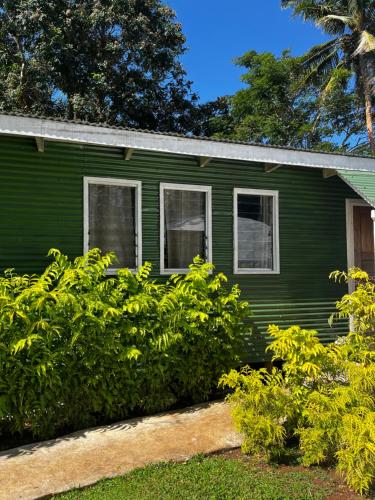 a green house with white windows and bushes at Camp Taveuni in Matei