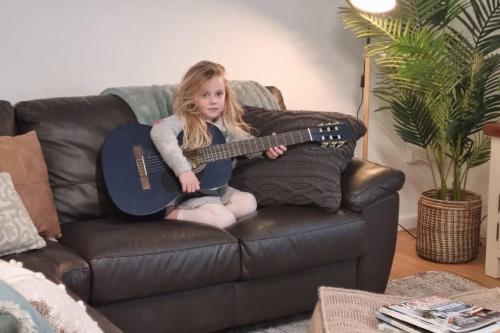 a little girl sitting on a couch playing a guitar at Sabi Robe WiFi 300m to Beach Dog friendly in Robe