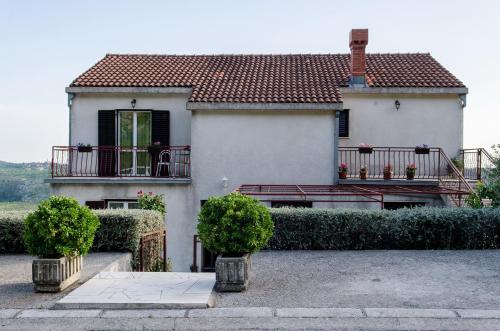 a white house with a balcony and two bushes at Olive Garden Apartments in Čilipi