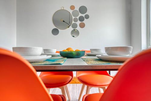 a dining room table with orange chairs and a clock on the wall at Abbey Court - 2 Bedroom Apartment, Parking, CVT, JLR in Coventry