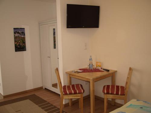 エアフルトにあるGästehaus in der Gotthardtstraßeのテーブルと椅子2脚、壁掛けテレビが備わる客室です。