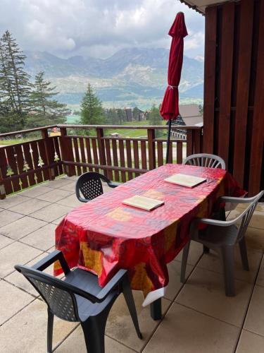ein roter Tisch mit Stühlen und einem Sonnenschirm auf einer Veranda in der Unterkunft l'appart accès direct sur les pistes in Le Dévoluy