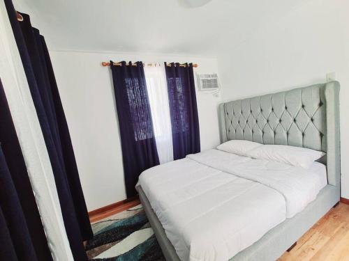 a bedroom with a bed with a gray headboard and curtains at Elon's Place in Catarman