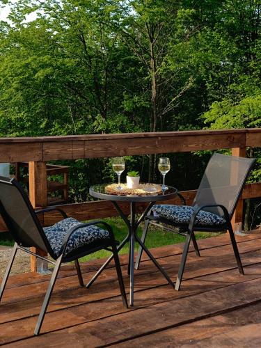 a table and two chairs on a deck with wine glasses at Sanctum Glamping in Jupâneşti