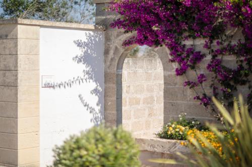 eine Steinmauer mit lila Blumen darauf in der Unterkunft Borgo Mulino a Vento - Resort in Uggiano la Chiesa