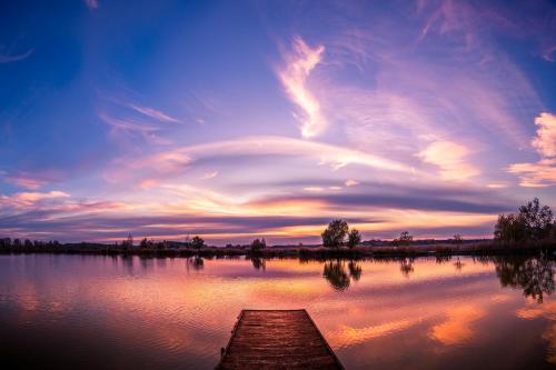 a lake with a pier and a cloudy sky at Holdruta Vendégház in Kunfehértó