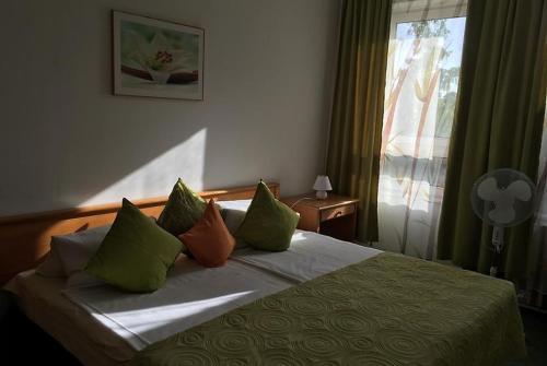 1 dormitorio con 1 cama con almohadas de color verde y naranja en Fenyves Szálló, en Balatonfenyves