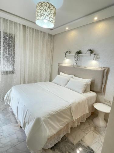 a white bedroom with a large bed and a chandelier at Studio SvEt 39 in Mohammedia