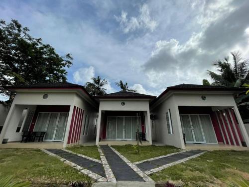 a house with red and white doors and grass at PONDOK SAHANG COTTAGES in Muntok