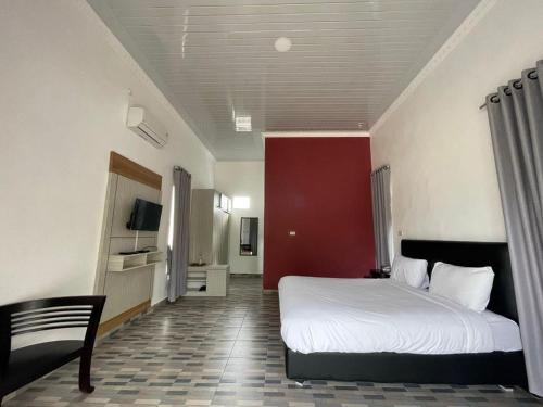 PONDOK SAHANG COTTAGES في Muntok: غرفة نوم بسرير ابيض وجدار احمر