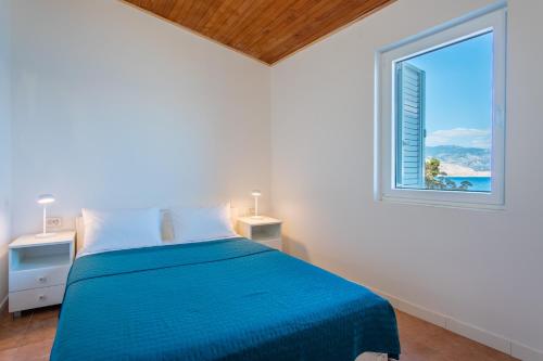 a white bedroom with a blue bed and a window at Villa Sortis in Pag