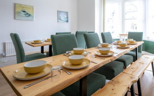 uma sala de jantar com uma longa mesa de madeira e cadeiras verdes em The Cadnant Holiday House em Llandudno