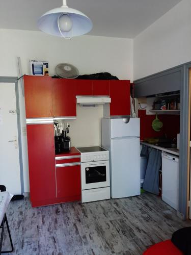 Elle comprend une petite cuisine avec des placards rouges et un réfrigérateur blanc. dans l'établissement Bel appartement-terrasse Ronce-les-Bains, à La Tremblade