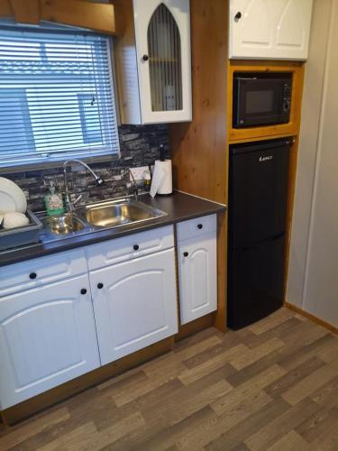 a kitchen with white cabinets and a sink and a microwave at L3 Millfields 4 Berth Luxury Caravan DG & GCH Family's Only And Lead Person Must Be Over 30 in Ingoldmells