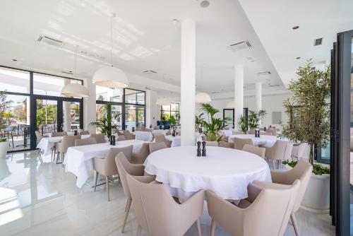 a dining room with white tables and chairs and windows at Miramare Hotel in Zadar