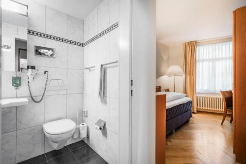 a bathroom with a toilet and a sink and a bed at Hotel Blume - Swiss Historic Hotel in Baden