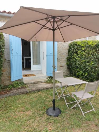 a table and two chairs under an umbrella at L'enclos bleu, gîte - marais poitevin avec piscine chauffée in Chaillé-les-Marais