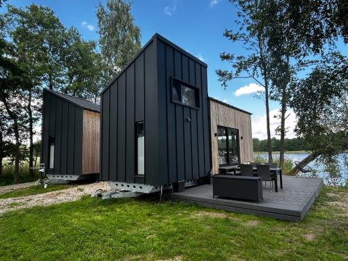 a black house with a deck next to a body of water at Tiny House - Osada Wilkasy in Giżycko