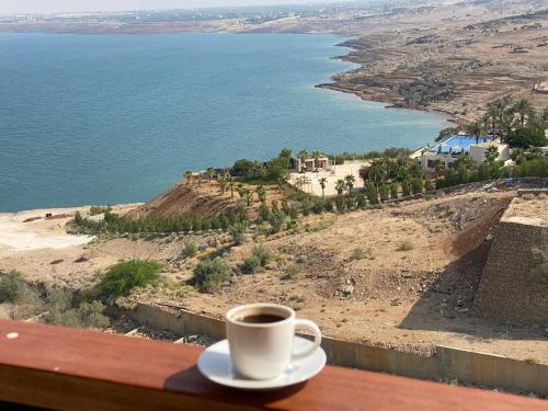 a cup of coffee sitting on a table next to the ocean at Dead Sea view Elite apartment Samara Resort traveler award 2024 in Sowayma