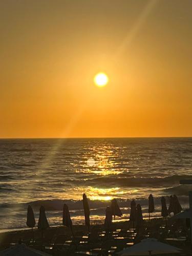 - un coucher de soleil sur la plage avec des parasols et l'océan dans l'établissement Cozy Corfu Bungalow 5 minutes to Aqualand, à Corfou