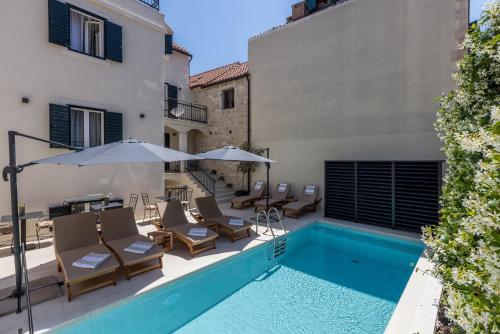 a pool with chairs and umbrellas next to a building at Sperone Hotel in Split