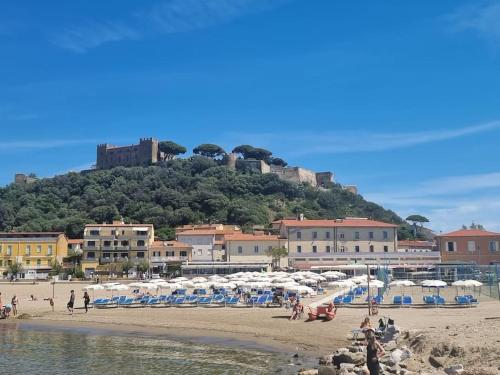 a beach with chairs and umbrellas and a castle on a hill at Casa Bortoli in Castiglione della Pescaia